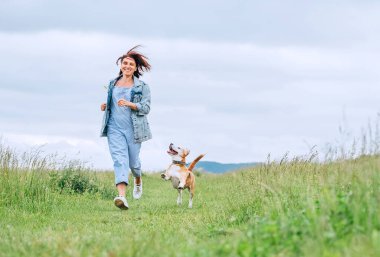 Mutlu, gülümseyen, saçları titreyen ve av köpeği koşan ve gözlerine bakan bir kadın. Doğada çayırlarda hayvanlarla yürümek, sağlıklı aktif insanlar yaşam tarzı imajı..