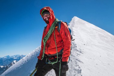 Mont Blanc (Monte Bianco) zirvesinden önceki son adımlar 4808 metre ip takımı mutlu gülümseyen adam tırmanış takımında, kar yamaçlarında mavi gökyüzü arka planına sahip kırmızı dağ kıyafetleri içinde..