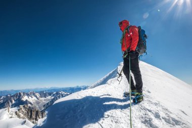 Mont Blanc (Monte Bianco) zirvesinden önceki son adımlar 4.808 m ip ekibi baltayla dağcılık kıyafetleri giymiş, kramponlu botlar mavi gökyüzü arkaplanlı karlı yamaçlarda yürüyor.