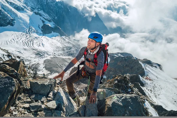 Emniyet kemeriyle tırmanan, sırt çantalı, arka planda Bionnassay Buzulu olan bir kaya duvarına tırmanan ve Fransa 'nın yükselen Mont Blanc zirvesine bakan bir adam. Etkin tırmanma kavramı.