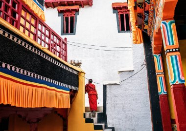 Monastery in Thiksey village, India  August 20, 2016: Young monk boy goes by the monastery weared in traditional red kasaya  in Thiksey village, India clipart