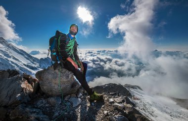 Emniyet kemeri, miğfer ve yüksek dağcı botları ile tırmanan büyük bir kaya üzerinde 3600 metre yükseklikte oturan ve Fransa 'nın yükselen Mont Blanc zirvesine bakan