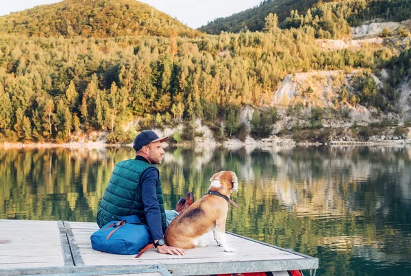 在秋天的时候 狗的主人和他的朋友小猎犬正坐在山上湖上的木制码头上散步 欣赏风景 人类和宠物的概念形象 — 图库照片