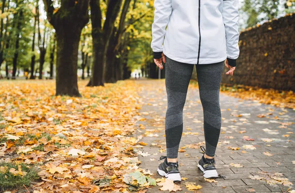 若いフィット運動選手の女性は 秋の都市公園でジョギングする前に 歩道に立って現代的なランニング服を着ています 実行中の人のコンセプトイメージ — ストック写真