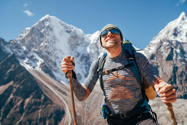 Portrait of smiling Hiker man on Taboche 6495m and Cholatse 6440m peaks background with trekking poles, UV protecting sunglasses. He enjoying mountain views during Everest Base Camp trekking route.