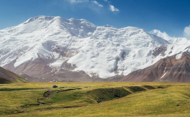 Yeşil çimen dağ vadisinde, Pamir dağlarının derinliklerinde tepelerle çevrili, arka planda Lenin tepesi 7134 metre, Kırgızistan, Orta Asya