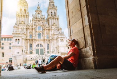 Santiago de Compostela 'daki Obradoiro Meydanı' nda Santiago de Compostela Katedrali 'nin ünlü Camino de Santiago bitiş noktasında oturan orta yaşlı gezgin yorgun.