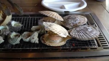 Çeşitli türlü ızgara deniz kabukları scallop(Hotate), boynuzlu türban deniz salyangoz (Sazae) ve Wakayama balık pazarı, Japan.Roasted balık duman ile sıcak ızgara balık.