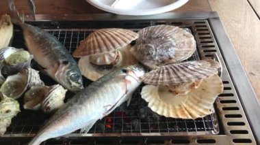Çeşitli türlü ızgara deniz kabukları scallop(Hotate), boynuzlu türban deniz salyangoz (Sazae) ve Wakayama balık pazarı, Japan.Roasted balık duman ile sıcak ızgara balık.