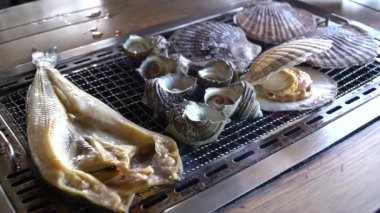 Çeşitli türlü ızgara deniz kabukları scallop(Hotate), boynuzlu türban deniz salyangoz (Sazae) ve Wakayama balık pazarı, Japan.Roasted balık duman ile sıcak ızgara balık.
