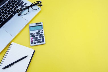 Üstten görünüm office tablo resepsiyon. Tablo çalışma alanıyla ofis aksesuarları dahil olmak üzere dizüstü bilgisayar, defter, kalem, hesap makinesi, sarı zemin üzerine glasse. Metin için yer kopyalayın. Word boş boş sayfa. Düz yatıyordu 