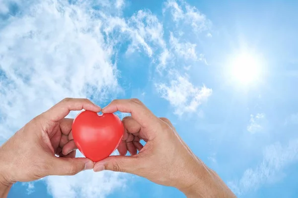 Man hold hands up to sky in the shape of love heart with red heart on nature sunlight flare and cloud.Valentine\'s day,Sign of Love,Health care,Valentine\'s day,World heart day Concept.