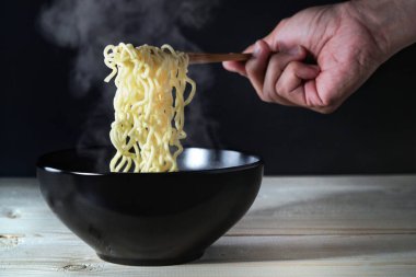 Ahşap çubuk duman ile anlık erişte tutan el. Sıcak çorba kase seçici odak Buhar. Anlık erişte mi uygun, lezzetli ve ucuz gıda.