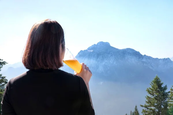 Woman lifting a glass of beer and drinking draft beer.happy enjoying harvest time at outdoor on beautiful mountain scene background.Celebration drinking beer.