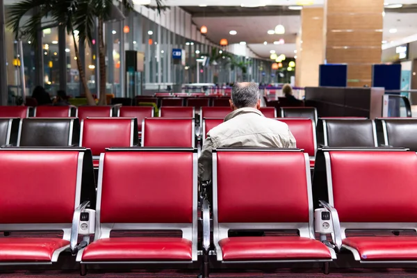 Passenger seat in departure to waiting for flight aircraft.Muture businessman traveller sitting on a bench in airport terminal waiting for the plane at boarding gate.Travel Vacation Holiday Concept.