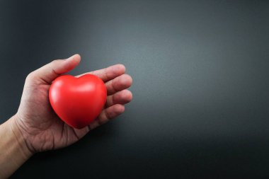 Man El tutan Kırmızı Kalp, Sevgi ve Sağlık Kavramı, aile sigortası. Dünya kalp günü, Dünya sağlık günü. Sevgililer Günü.siyah arka plan üzerinde kalbin izole şekli.