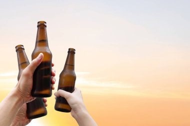 Eller üç bira şişesi tutan ve güzel günbatımı arka plan açık partide gözlük klinking için birlikte hasat zaman zevk. Kutlama başarı içme bira.       