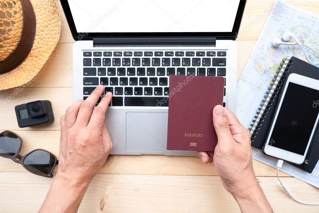 Hand holding passport with a map and laptop for planning to travel.Top view of traveler accessories with a hat, camera, watch on world map.Traveling Journey Vacation Holiday concept.