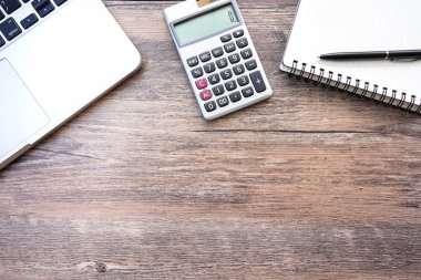 Düz konum, üst görünüm ofis masası. Hesap makinesi, kalem, dizüstü bilgisayarı olan çalışma alanı eski ahşap arka planda. Metin için boşluk, sözcük için boşluk kopyala. İş Finansmanı, Eğitim Teknolojisi. Evden çalışma..