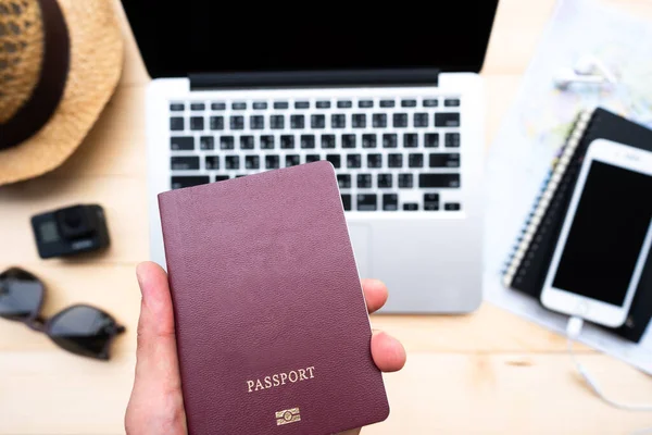 Hand holding passport with a map and laptop for planning to travel.Top view of traveler accessories with a hat, camera, watch on world map.Traveling Journey Vacation Holiday concept.