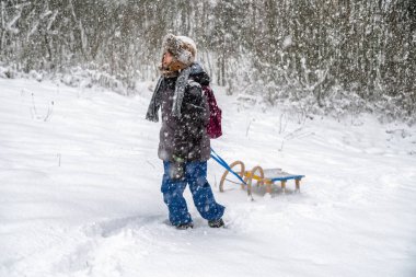 Çocuk karlı ormandaki bir kızak çekme