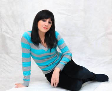 Genç güzel bir kadının portresi, minimal makyaj, doğallık ve güzellik ile pürüzsüz sağlıklı bir cilt. Gri bir arka plan üzerinde Büyüleyici esmer, katta oturan.