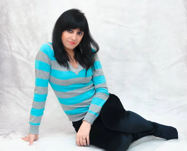 Genç güzel bir kadının portresi, minimal makyaj, doğallık ve güzellik ile pürüzsüz sağlıklı bir cilt. Gri bir arka plan üzerinde Büyüleyici esmer, katta oturan.