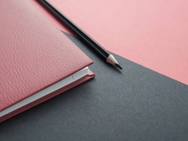 Office accessories: Red notepad, pencil on a red-black background. Top view. Copy space.