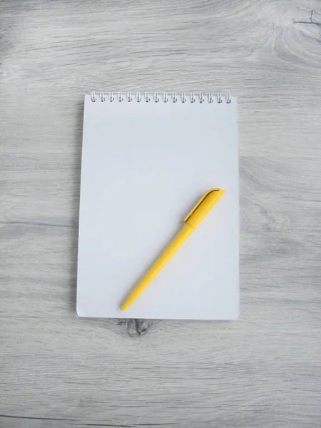 Acessórios de escritório: caneta amarela, bloco de notas em branco em uma mesa cinza de madeira. Vista superior. Espaço de cópia — Fotografia de Stock