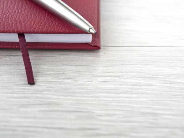 Accesorios de oficina: Un bloc de notas rojo y una pluma de metal sobre un escritorio gris de madera. Vista superior. Copiar espacio —  Fotos de Stock