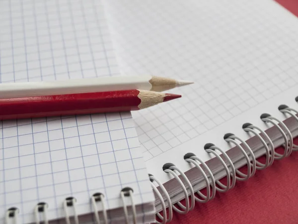 Kantoorbenodigdheden: een stapel witte notebooks, witte potlood, rode potlood op een rode achtergrond. Onderwijs. Business. Het concept. Bovenaanzicht. Kopieer ruimte. ? verliezen Stockfoto