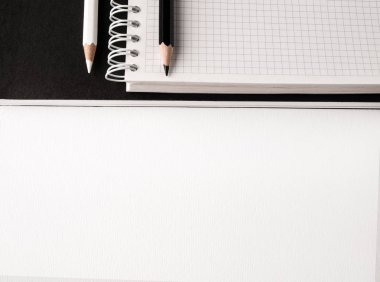 Ofis konsepti. Beyaz Kağıt arka planda siyah ve beyaz kalemler, boş defter ve siyah dergi. Üst görünüm. Boşluk Kopyala