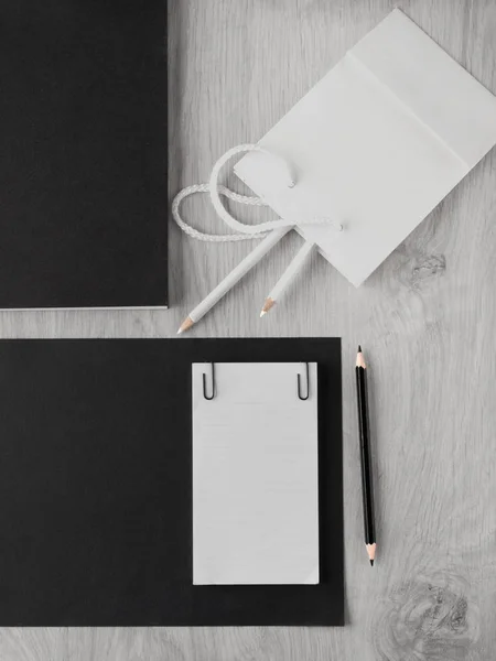 Pracovní stůl: papír, tužka, deník, černá lepenka, bílý papírový sáček s tužkami na dřevěném šedém stole. Pohled shora. Kopírovat místo — Stock fotografie