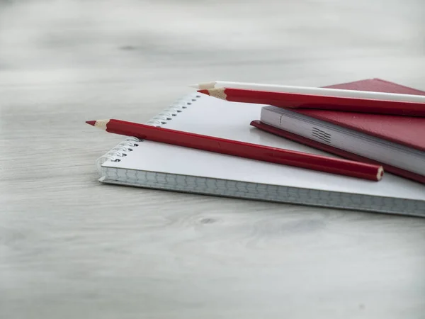 Офісні аксесуари: червоний блокнот, білий блокнот та олівці на дерев'яному сірому столі. Повернутися до школи. Замовкни. Вид зверху. Копіювати простір — стокове фото