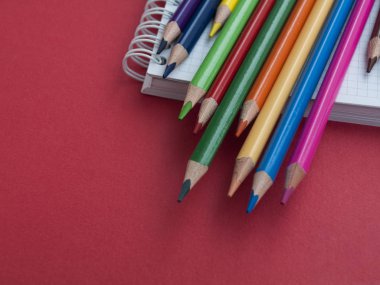 Okul ve ofis malzemeleri: renkli kalemler ve kırmızı kağıt arka plan üzerinde bir defter. Üst te. Close