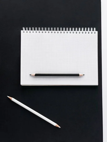 Kontors koncept. Svarta och vita blyertspennor, tom anteckningsbok på svart pappers bakgrund. Översta vyn. Kopiera utrymme — Stockfoto