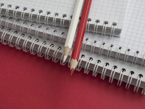 Fournitures de bureau : une pile de cahiers blancs, crayon blanc, crayon rouge sur un fond rouge. L'éducation. Les affaires. Le concept. Vue de dessus. Espace de copie. ? perdre-up — Photo