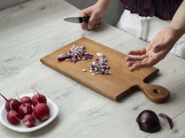 Sağlıklı beslenme: eller kırmızı soğanı keser, turp da tahta gri bir masada. Üst görünüm