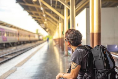 bir gezgin, rahat kıyafetler ve güneş gözlüğü ile fotoğraf makinesi, oturma ve bir tren platformu için bekleyen backpacker adam Tren İstasyonu