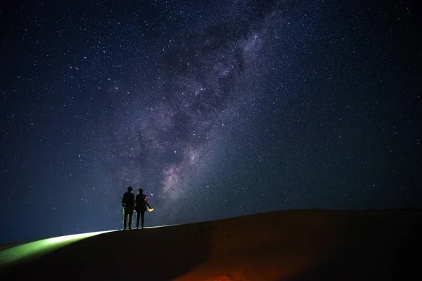 Landscape with Milky Way. Night sky with stars and silhouette of a standing  couple on sand hill.