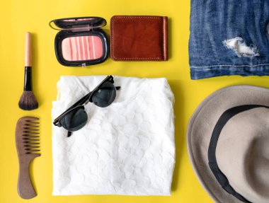 üstten görünüm düz tabaka seyahat yaşam tarzı güzellik ile yapmak küme, maskara, fırçalar, göz farı damak ve fırça, yırtık kot, güneş gözlüğü ve şapka sarı zemin üzerine