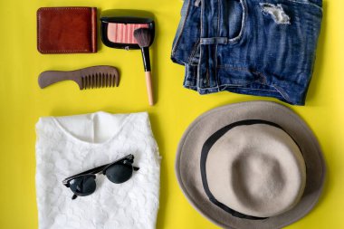 üstten görünüm düz tabaka seyahat yaşam tarzı güzellik ile yapmak küme, maskara, fırçalar, göz farı damak ve fırça, yırtık kot, güneş gözlüğü ve şapka sarı zemin üzerine