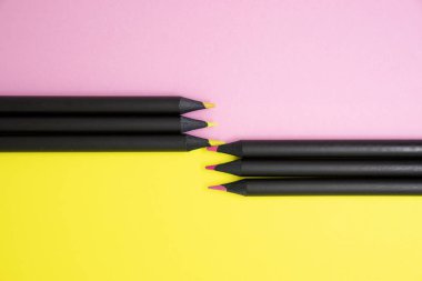 Siyah renkli kalemler üst görüşlerini pembe ve sarı renkli kağıt arka plan kopya alanı ile üzerinde tonlarında renkli.