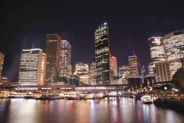 limana yansıma ile Circular Quay iskelede aydınlatılmış bina şehir ve Tren İstasyonu manzarası. Circular Quay bir ağ geçidi olarak hizmet vermektedir, ziyaretçilerini Major 'un cazibe merkezlerine bağlayan Avustralya: 10/04/18