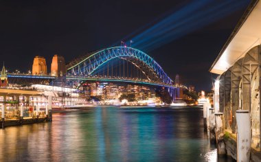 Avustralya-Sydney: Haziran 07, 2017. Circular quay wharf görünümünden Sydney Harbour Bridge parlak canlı Sydney Festivali sırasında 2017 bulanık liman sularda yansıtan ışık ile aydınlatılmış..
