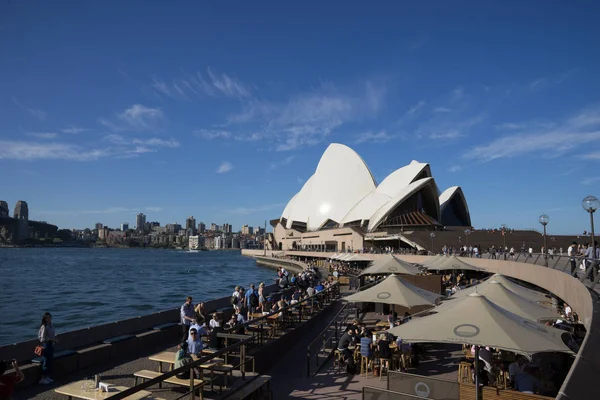 Gezginler ve yerel halkın içki içip Opera Binası önünde, Opera barda güzel bir açık mavi gökyüzü güneşli günün tadını çıkarın. Avustralya: 28/02/18