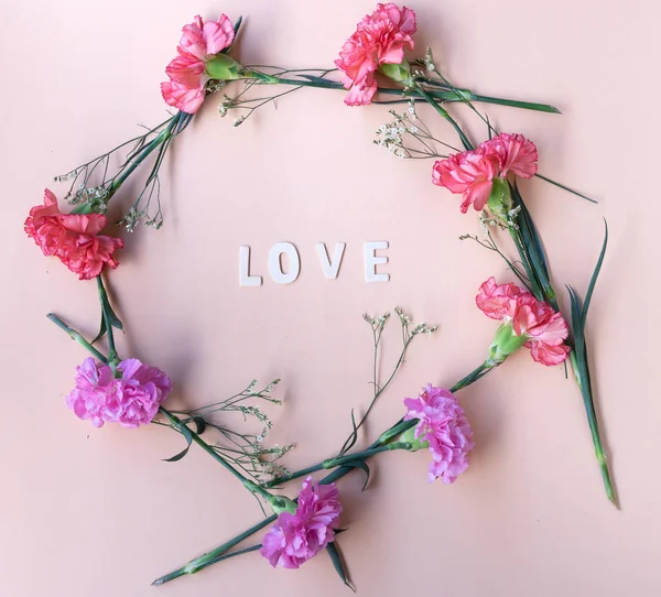 love wooden word  with fresh flowers geometric frame on  pale pink background