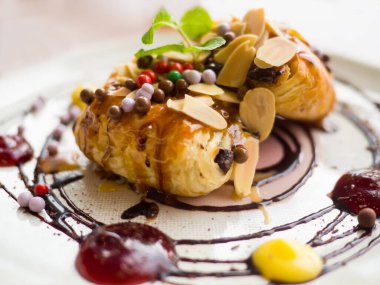 Şuruplu Danimarka pastası, badem ve çikolata topları serpiştirilmiş. Etrafında reçel olan beyaz bir tabak koy..