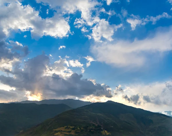 Mavi gökyüzünde bulutlar vurgulu ise dağlar arkasına saklanmış güneş