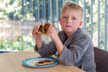 Genç çocuk onun sabahlığını ile masada oturan kahvaltıda Vegemite tost yemek 